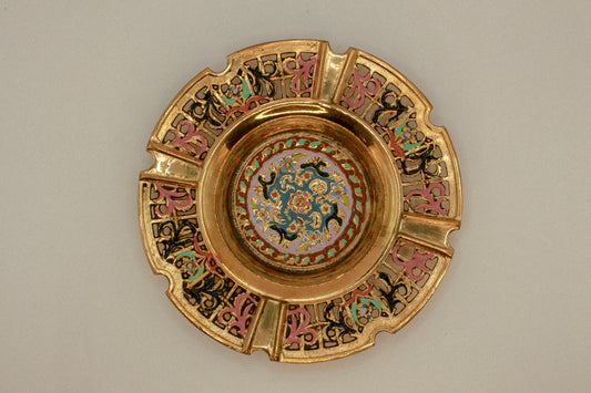 Decorative brass vintage ashtray with intricate painted designs on a green textured background