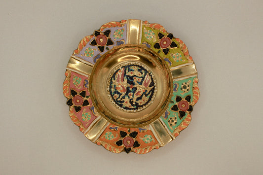 Decorative brass vintage ashtray with intricate painted designs on a green textured background