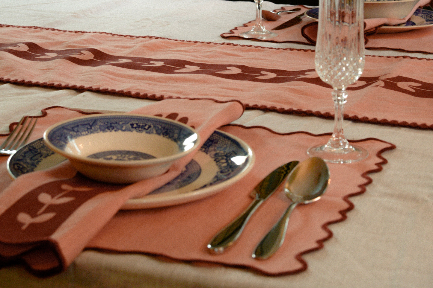 Dining table setting with pink placemats, blue and white bowl, silverware, and a glass.