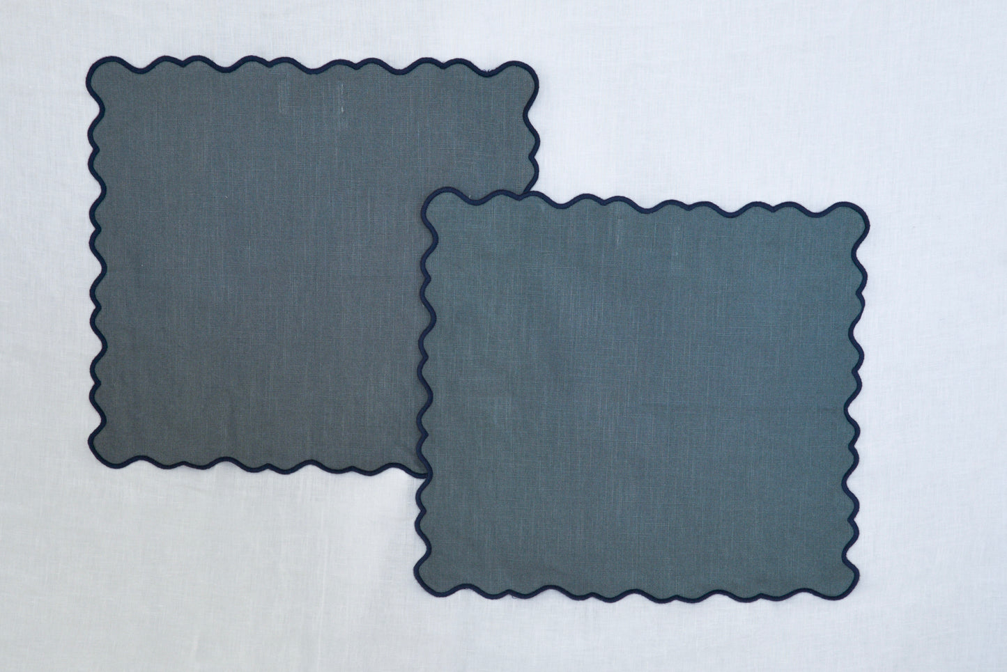 Two scalloped-edged dark blue placemats on a light gray background