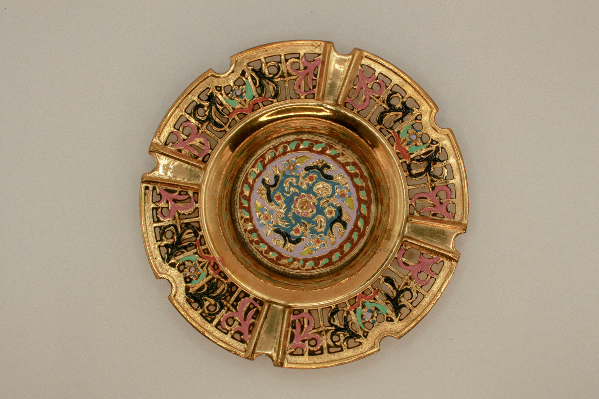 Decorative brass vintage ashtray with intricate painted designs on a green textured background