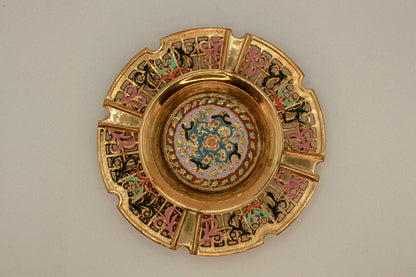 Decorative brass vintage ashtray with intricate painted designs on a green textured background