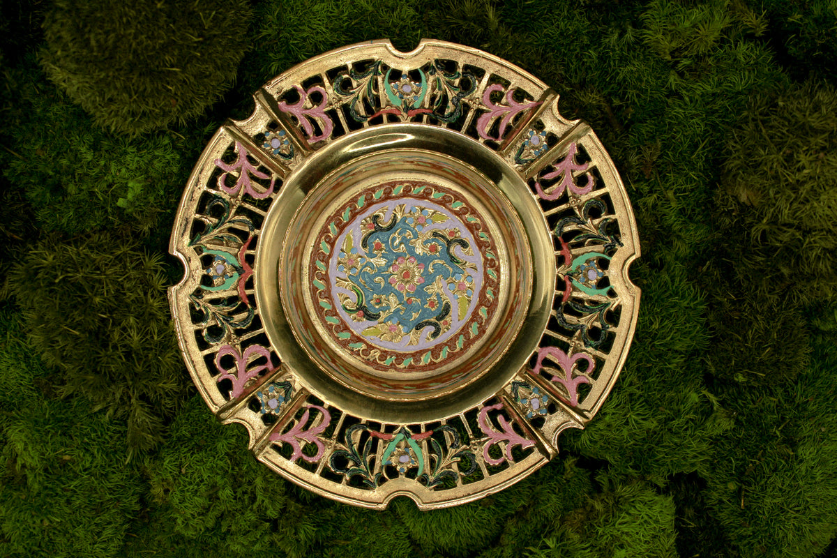 Decorative brass vintage ashtray with intricate painted designs on a green textured background