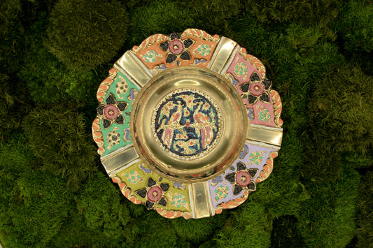 Decorative brass vintage ashtray with intricate painted designs on a green textured background