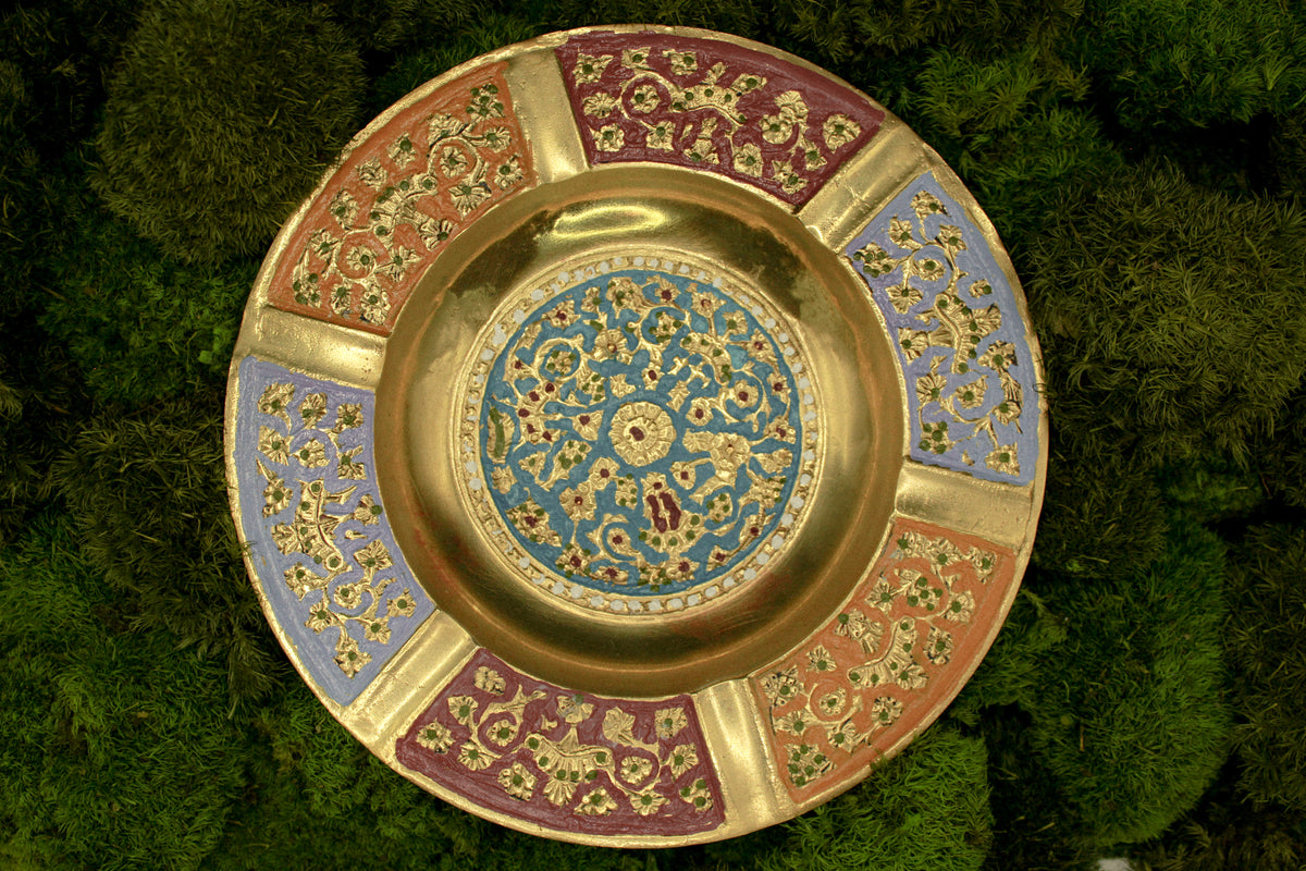 Decorative brass vintage ashtray with intricate painted designs on a green textured background