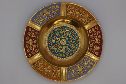 Decorative brass vintage ashtray with intricate painted designs on a green textured background