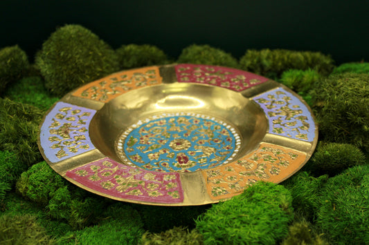 Decorative brass vintage ashtray with intricate painted designs on a green textured background