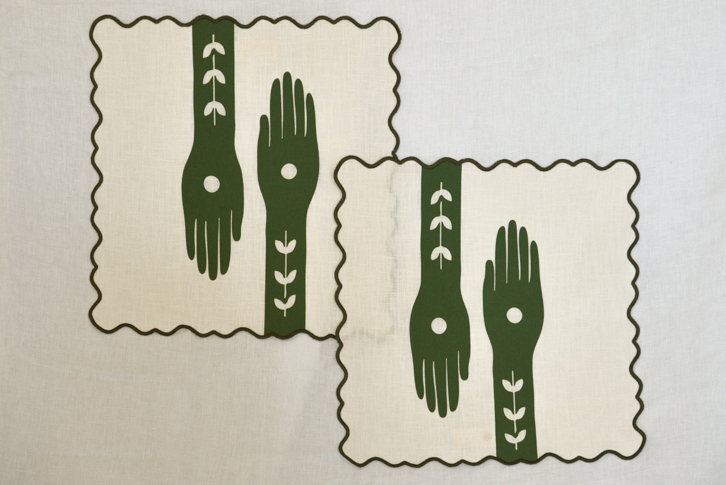 Two green placemats with hand designs on a beige background