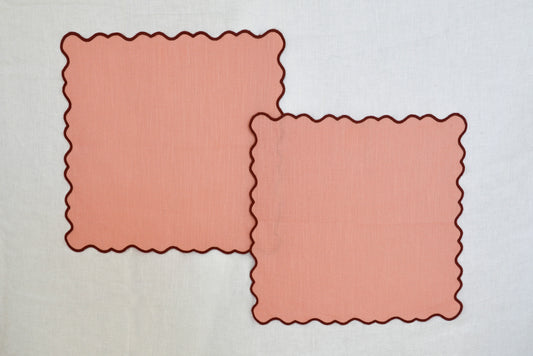 Two pink square linen/cotton blend placemats with scalloped edges on a light gray background