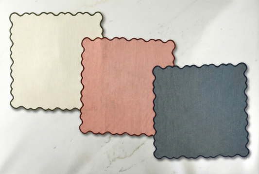 Three square placemats in beige, pink, and blue on a marble surface